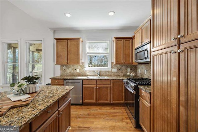 kitchen with appliances with stainless steel finishes, brown cabinets, a sink, light wood-style floors, and backsplash