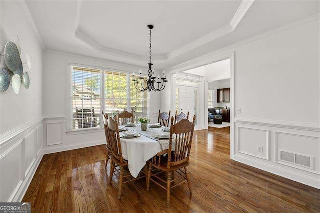 dining space with crown molding, a raised ceiling, visible vents, a decorative wall, and wood finished floors