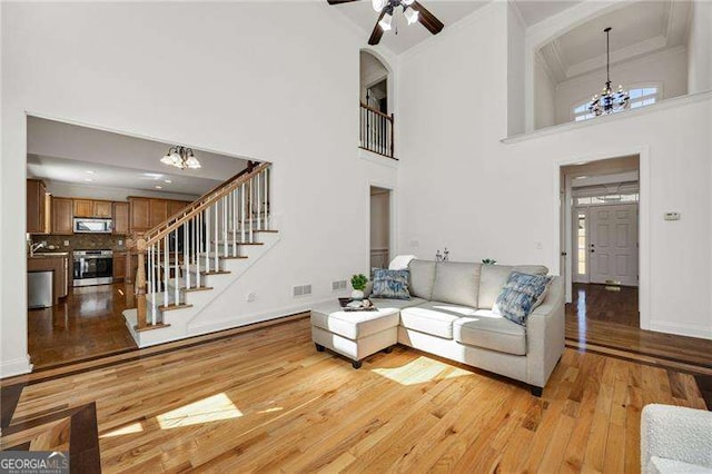 living room featuring visible vents, baseboards, stairs, light wood-style floors, and crown molding