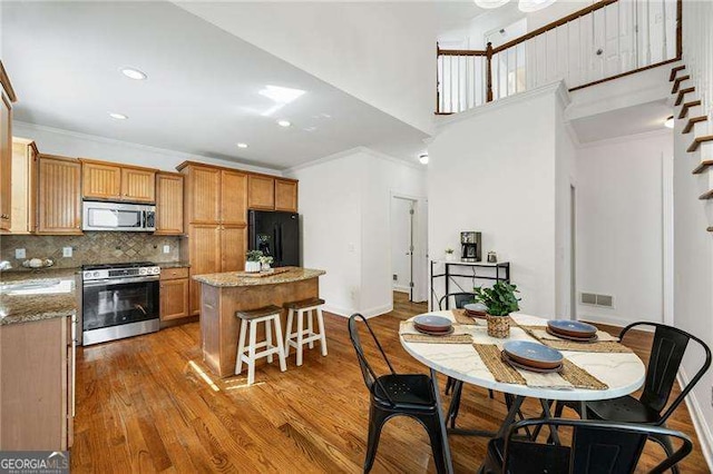 kitchen with tasteful backsplash, a kitchen island, appliances with stainless steel finishes, ornamental molding, and wood finished floors