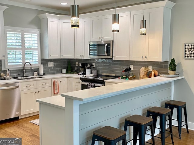 kitchen featuring light wood-style flooring, decorative backsplash, appliances with stainless steel finishes, a sink, and a peninsula