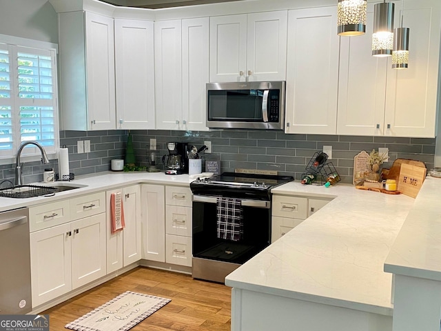 kitchen featuring light wood finished floors, stainless steel appliances, decorative backsplash, white cabinetry, and a sink