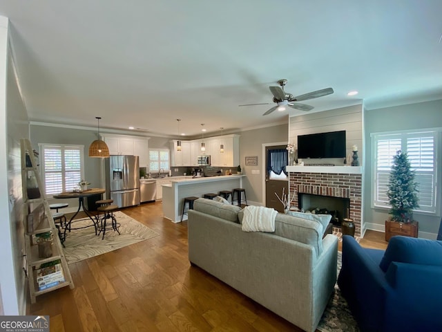 living room featuring dark wood-style floors, a brick fireplace, crown molding, and recessed lighting