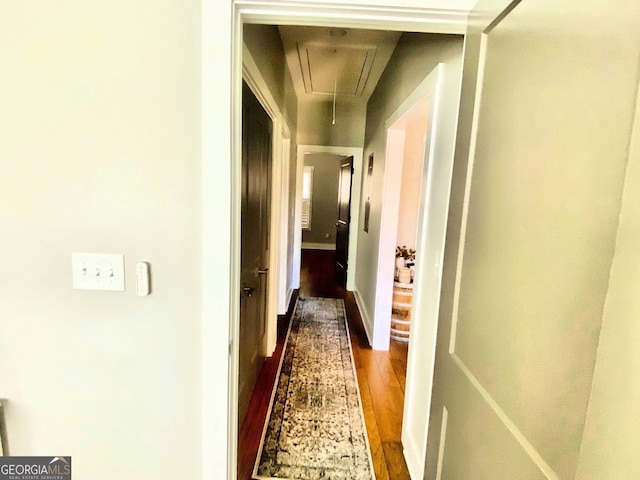 hallway featuring attic access, dark wood-type flooring, and baseboards