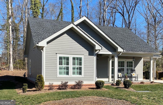 bungalow with a porch, roof with shingles, and a front lawn