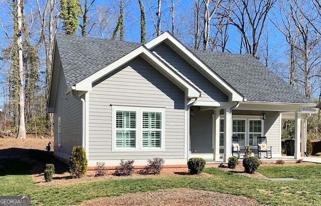 bungalow with a front yard, covered porch, and roof with shingles