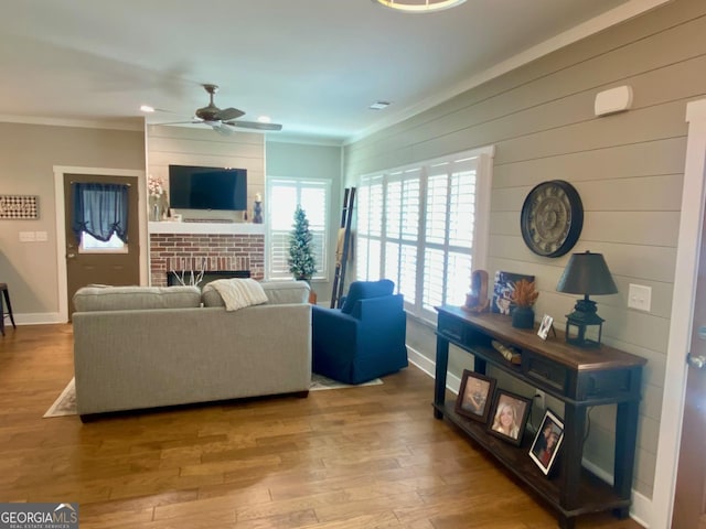 living area featuring ceiling fan, a fireplace, wood finished floors, baseboards, and ornamental molding