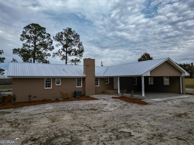 back of property featuring metal roof, central AC, brick siding, crawl space, and a chimney