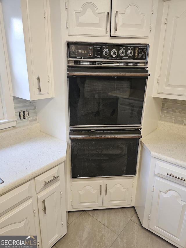 kitchen featuring light stone counters, decorative backsplash, white cabinetry, and dobule oven black