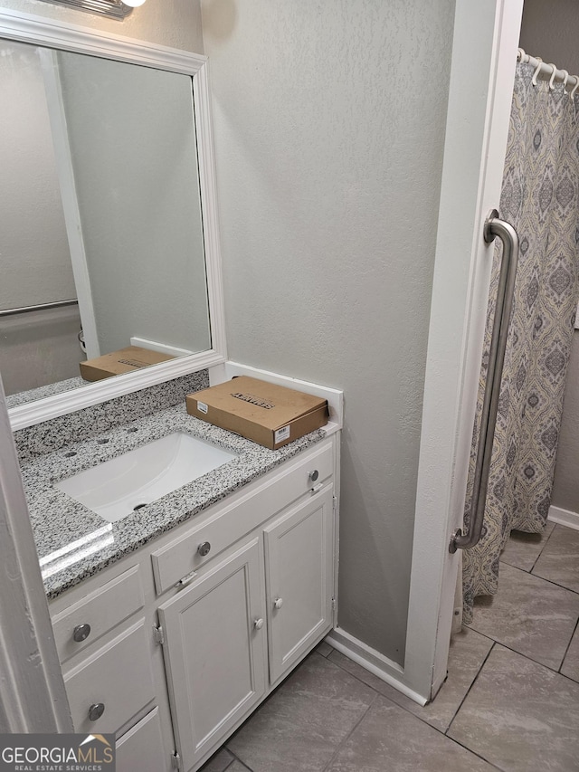 bathroom featuring a textured wall, curtained shower, vanity, and baseboards