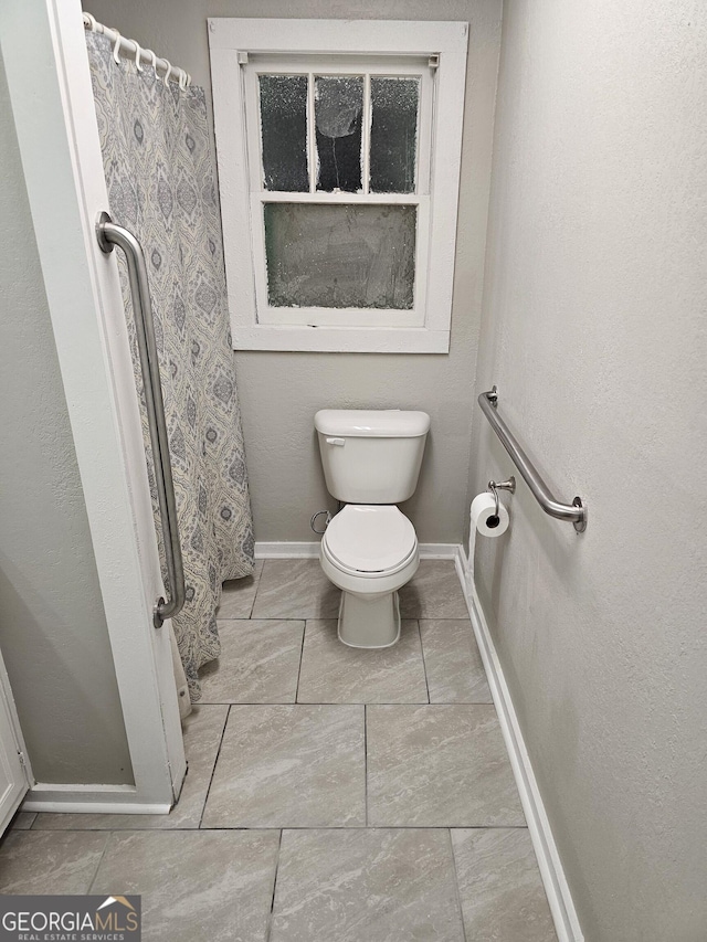 bathroom featuring toilet, curtained shower, and baseboards