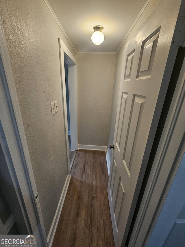 hallway with ornamental molding, a textured wall, baseboards, and dark wood-style floors