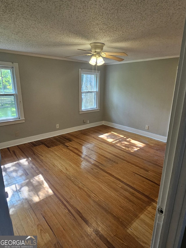 unfurnished room with crown molding, a ceiling fan, a textured ceiling, wood finished floors, and baseboards