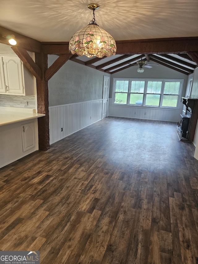 unfurnished living room with dark wood-type flooring, a wainscoted wall, vaulted ceiling with beams, and ceiling fan