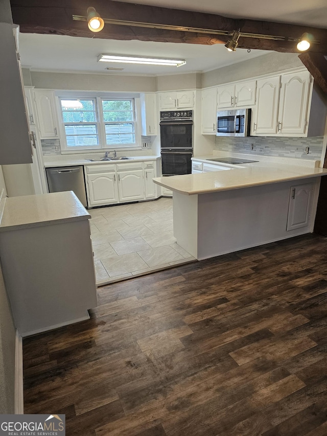 kitchen featuring decorative backsplash, a peninsula, black appliances, white cabinetry, and a sink