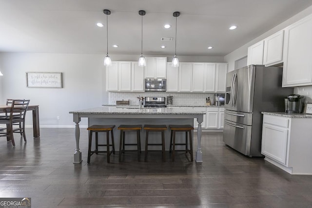 kitchen featuring tasteful backsplash, white cabinets, light stone counters, appliances with stainless steel finishes, and a breakfast bar area