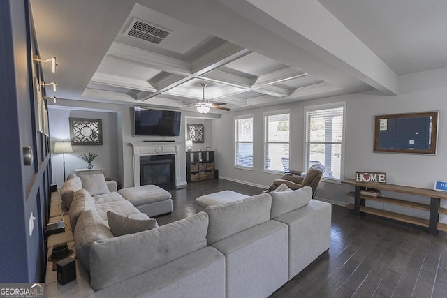 living area featuring visible vents, coffered ceiling, a glass covered fireplace, beamed ceiling, and dark wood-type flooring