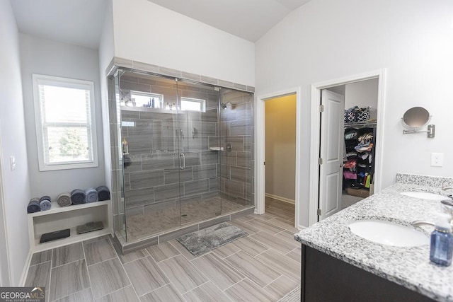 bathroom with a sink, baseboards, double vanity, a stall shower, and a walk in closet