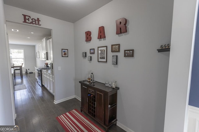 hall featuring dark wood-style floors, visible vents, and baseboards