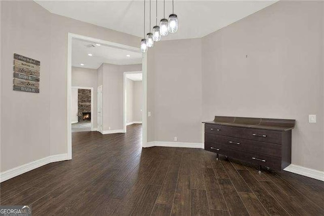 unfurnished dining area featuring dark wood finished floors, a stone fireplace, and baseboards