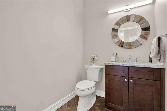 half bathroom featuring toilet, vanity, baseboards, and wood finished floors