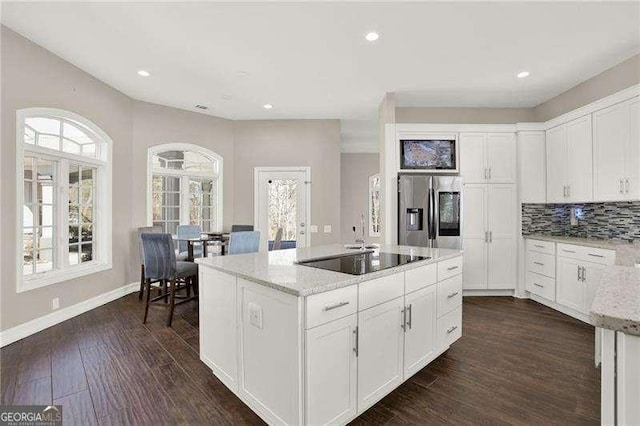 kitchen with dark wood finished floors, a center island, light stone countertops, black electric stovetop, and stainless steel refrigerator with ice dispenser