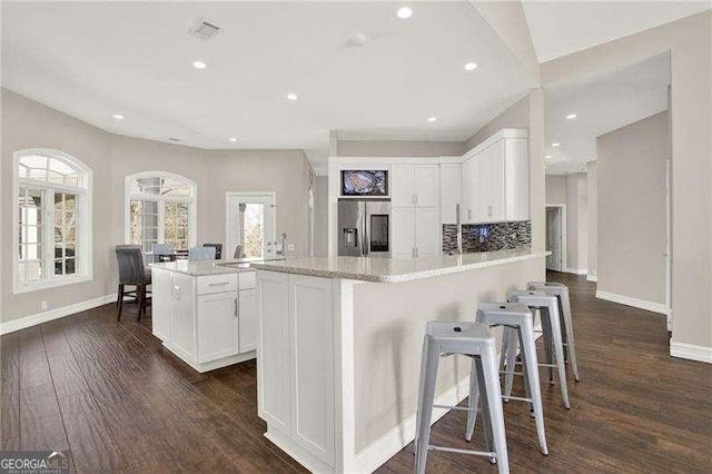 kitchen with a peninsula, plenty of natural light, stainless steel fridge, and white cabinets