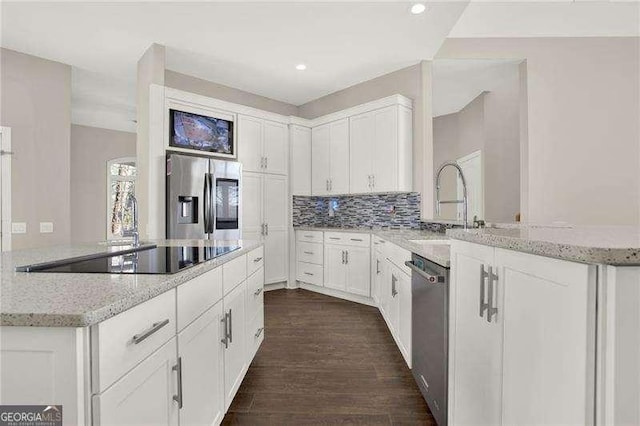 kitchen featuring light stone counters, dark wood-style floors, stainless steel appliances, white cabinetry, and a sink