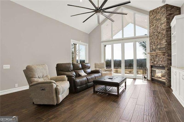 living room with baseboards, high vaulted ceiling, dark wood-style flooring, and a stone fireplace