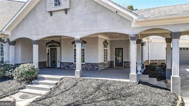 doorway to property featuring stone siding, a shingled roof, a porch, and stucco siding