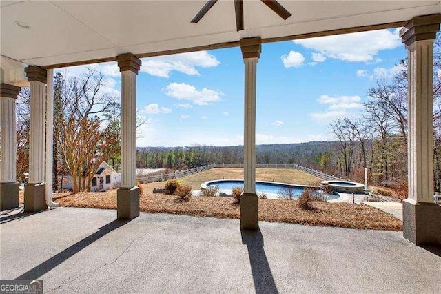 view of patio featuring a forest view, an outdoor pool, and a ceiling fan