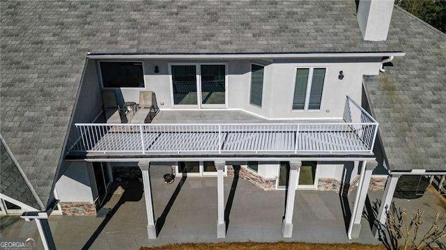 back of house featuring a shingled roof, a patio, a chimney, and stucco siding