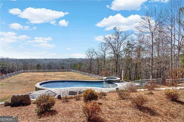 view of pool with an in ground hot tub, fence, and a view of trees