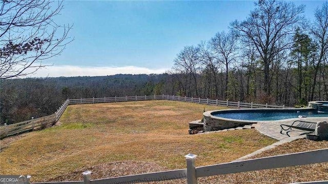 view of yard with a wooded view, fence, and an outdoor pool