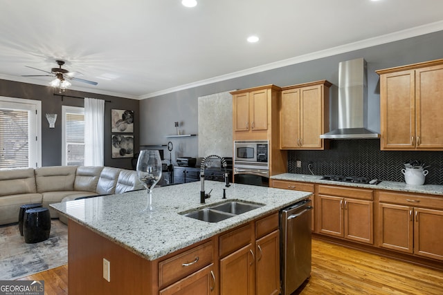 kitchen featuring crown molding, stainless steel appliances, open floor plan, a sink, and wall chimney range hood