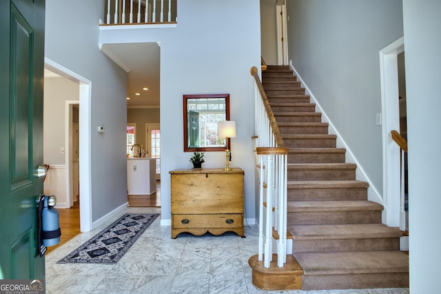 foyer entrance with a towering ceiling, crown molding, stairway, and baseboards