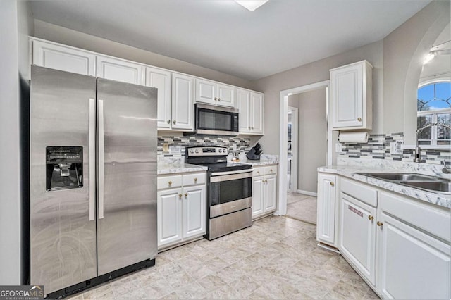 kitchen featuring white cabinets, a sink, light stone countertops, stainless steel appliances, and backsplash