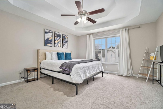 carpeted bedroom featuring ceiling fan, a raised ceiling, and baseboards