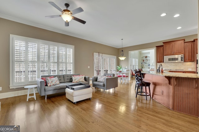 living area featuring ceiling fan, ornamental molding, light wood-type flooring, recessed lighting, and baseboards