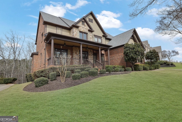 craftsman house with stone siding, brick siding, a porch, and a front lawn