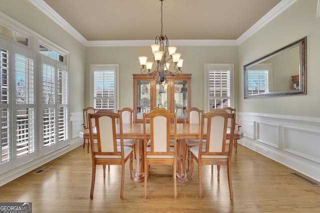 dining area with a chandelier, light wood finished floors, ornamental molding, wainscoting, and a decorative wall