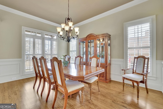 dining space with a chandelier, a wainscoted wall, healthy amount of natural light, a decorative wall, and crown molding