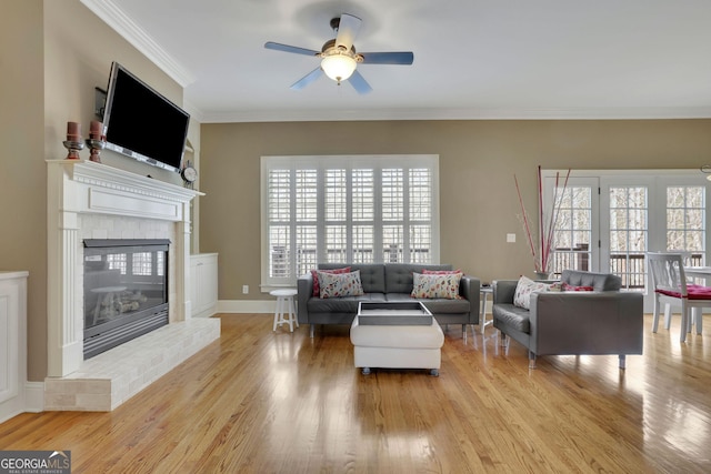 living room with healthy amount of natural light, a ceiling fan, light wood finished floors, a brick fireplace, and crown molding