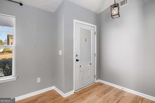 entryway with light wood-type flooring, visible vents, baseboards, and a textured ceiling