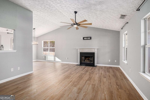 unfurnished living room with visible vents, a fireplace with flush hearth, ceiling fan, and wood finished floors