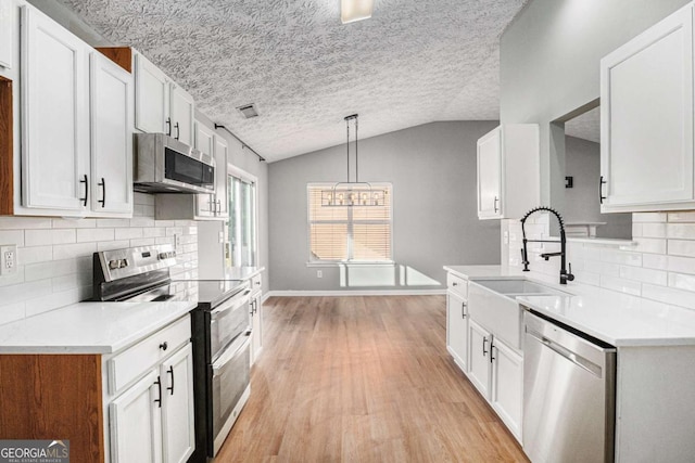 kitchen with light countertops, vaulted ceiling, light wood-style flooring, stainless steel appliances, and a sink