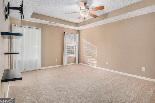 interior space with a raised ceiling, a textured ceiling, carpet floors, and a ceiling fan