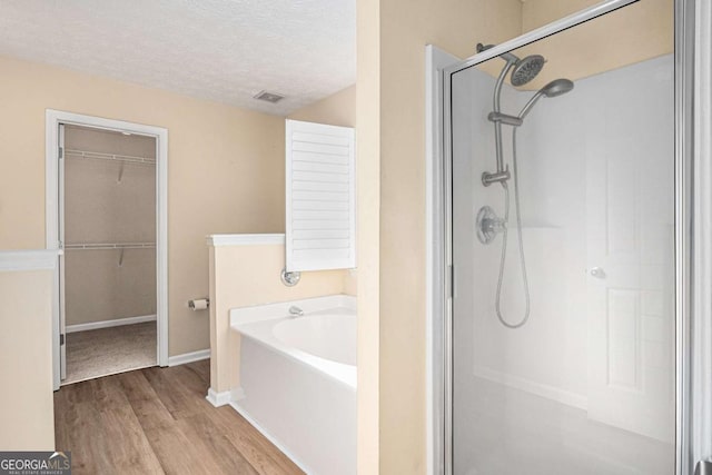 bathroom with visible vents, a walk in closet, a garden tub, a stall shower, and a textured ceiling