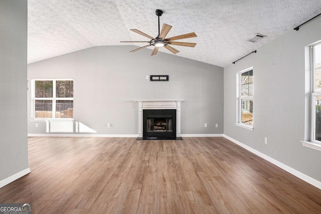 unfurnished living room featuring wood finished floors, a fireplace with flush hearth, a ceiling fan, and visible vents