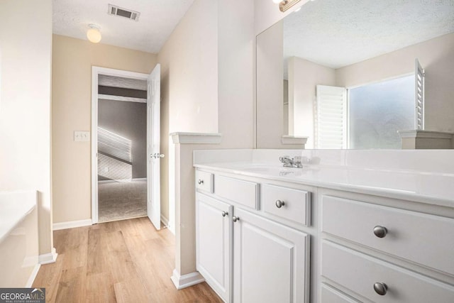 bathroom with vanity, wood finished floors, baseboards, visible vents, and a textured ceiling